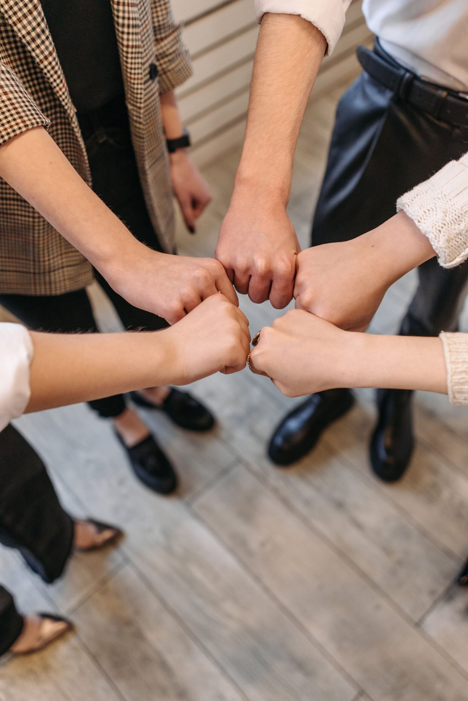 A close-up of five people fist bumping, symbolizing teamwork and unity indoors.